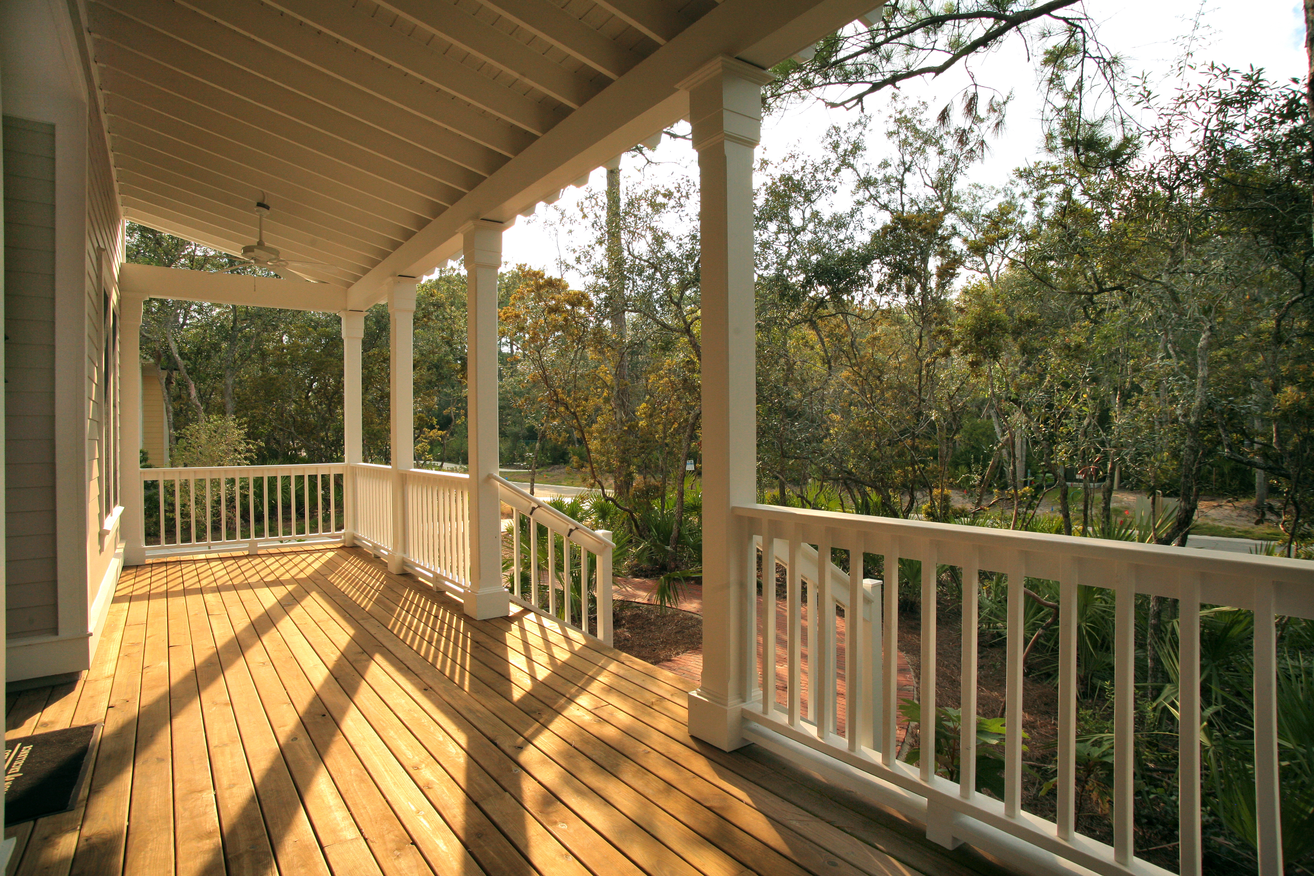 Spacious covered porch with white railings and wooden deck overlooking wooded landscape